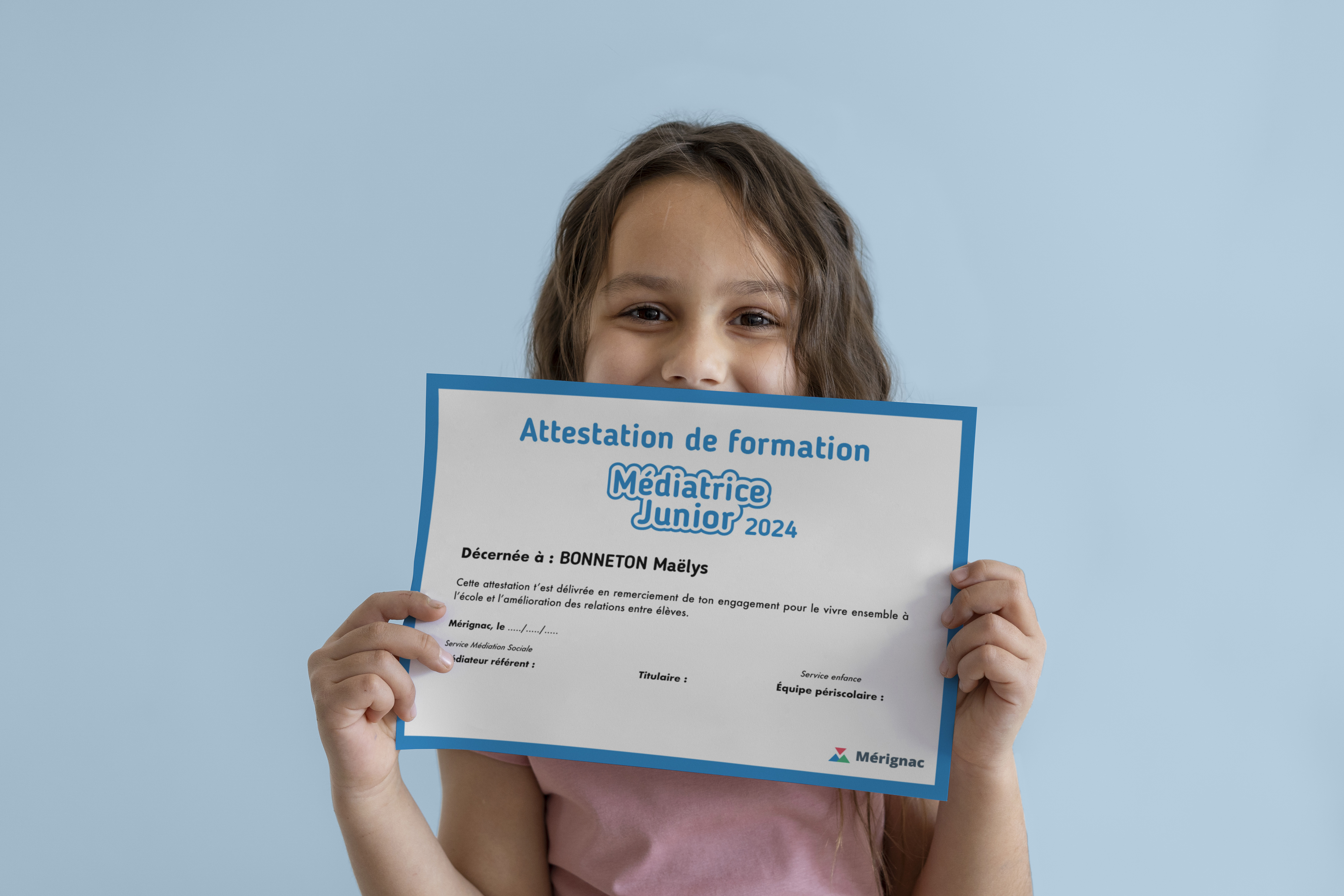 Une enfant montre fièrement son diplôme de "Médiatrice Junior", attribué par la ville de Mérignac.